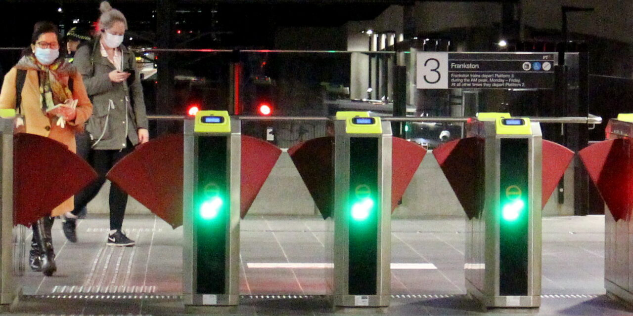 Railway station gates, passengers in masks